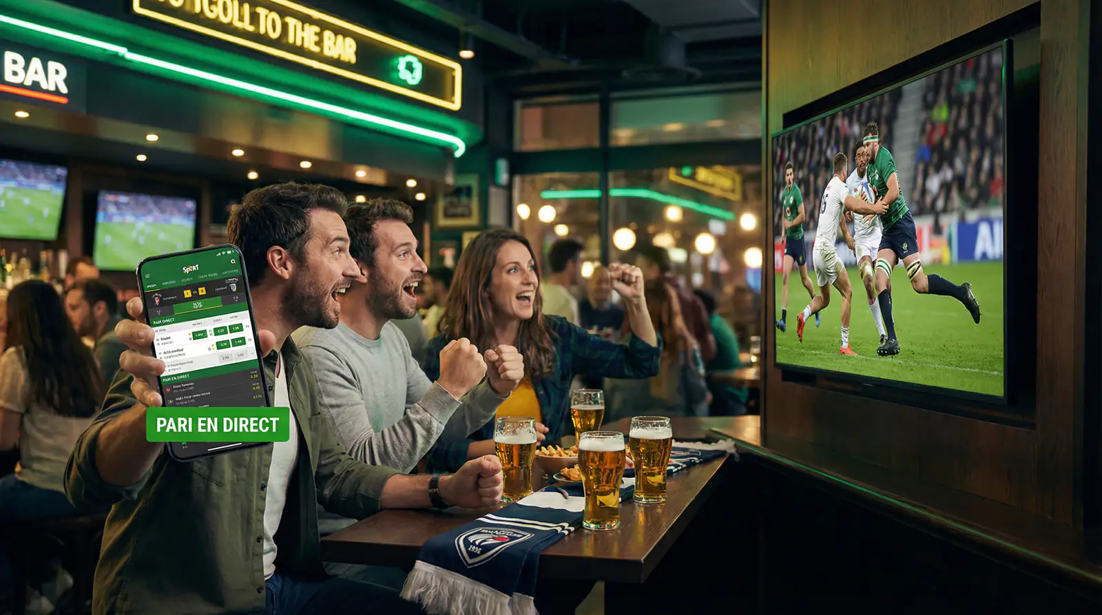 Groupe d'amis regardant un match de rugby dans un bar sportif tout en utilisant une application de paris en direct